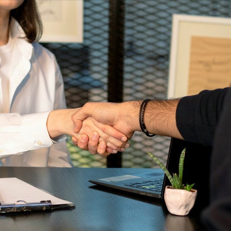 Händeschütteln zwischen zwei Personen am Tisch mit Pflanzen und Dokumenten.